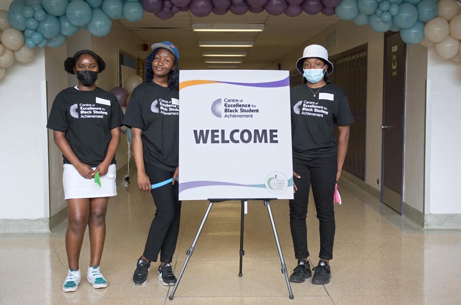 Three students stand beside the welcome sign. Open Gallery